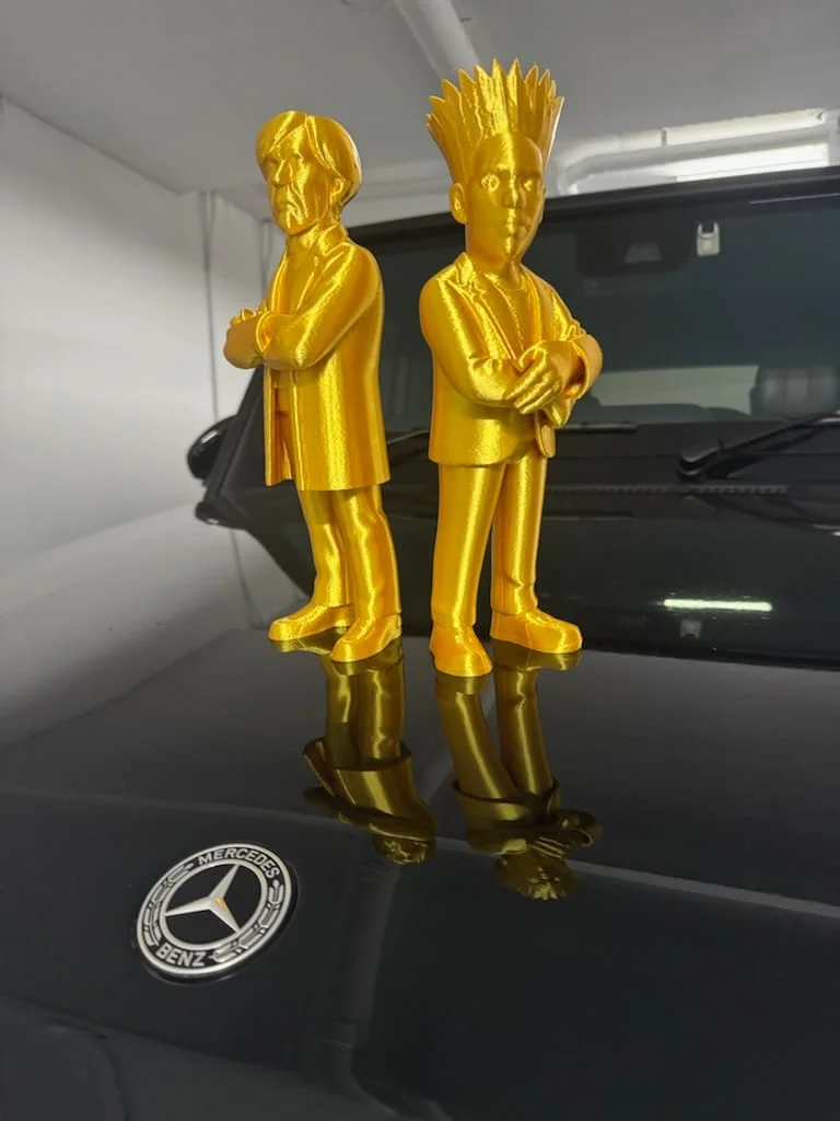 Two gold-coloured character sculptures standing on a car bonnet