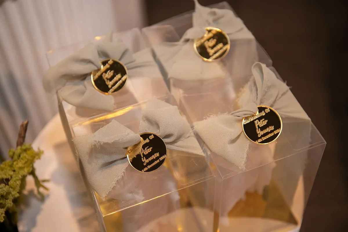 A group of clear favour boxes with white bows and personalised gold tags