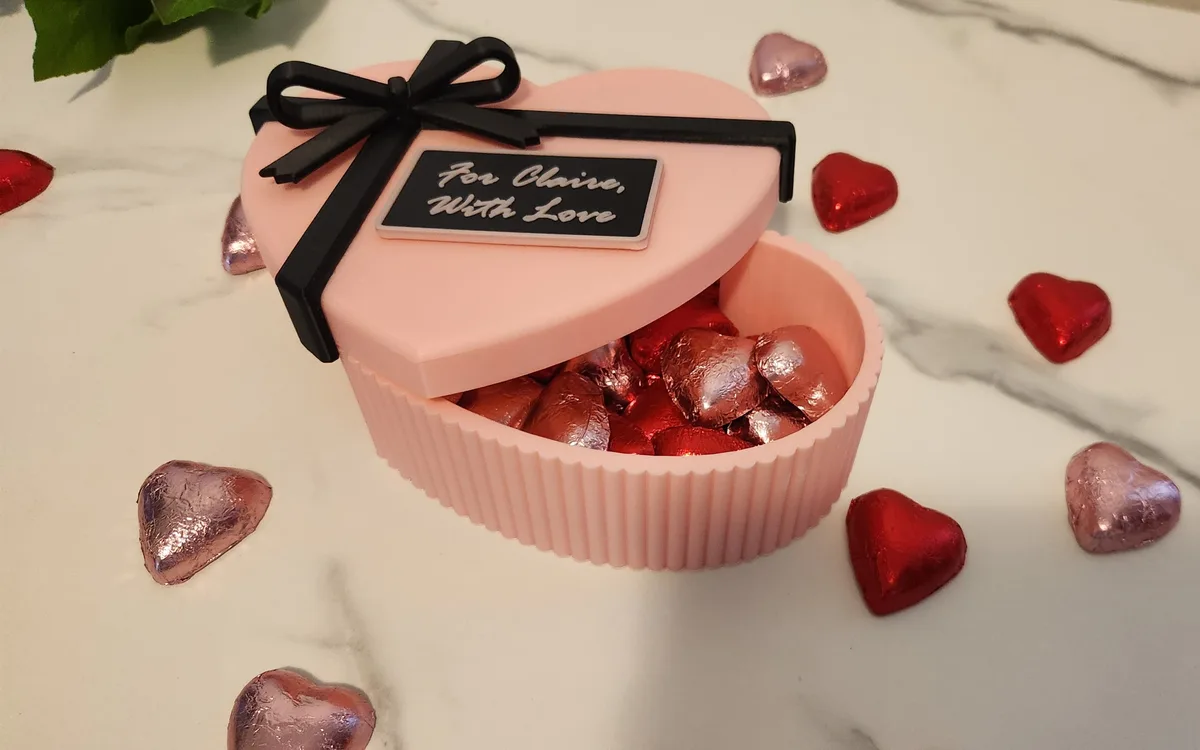 Pink heart-shaped gift box with a black ribbon and personalised message plaque