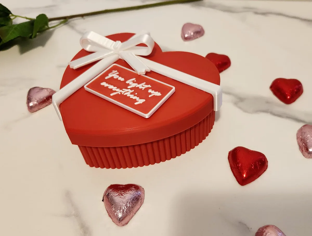 Red heart-shaped gift box with a white ribbon and message plaque