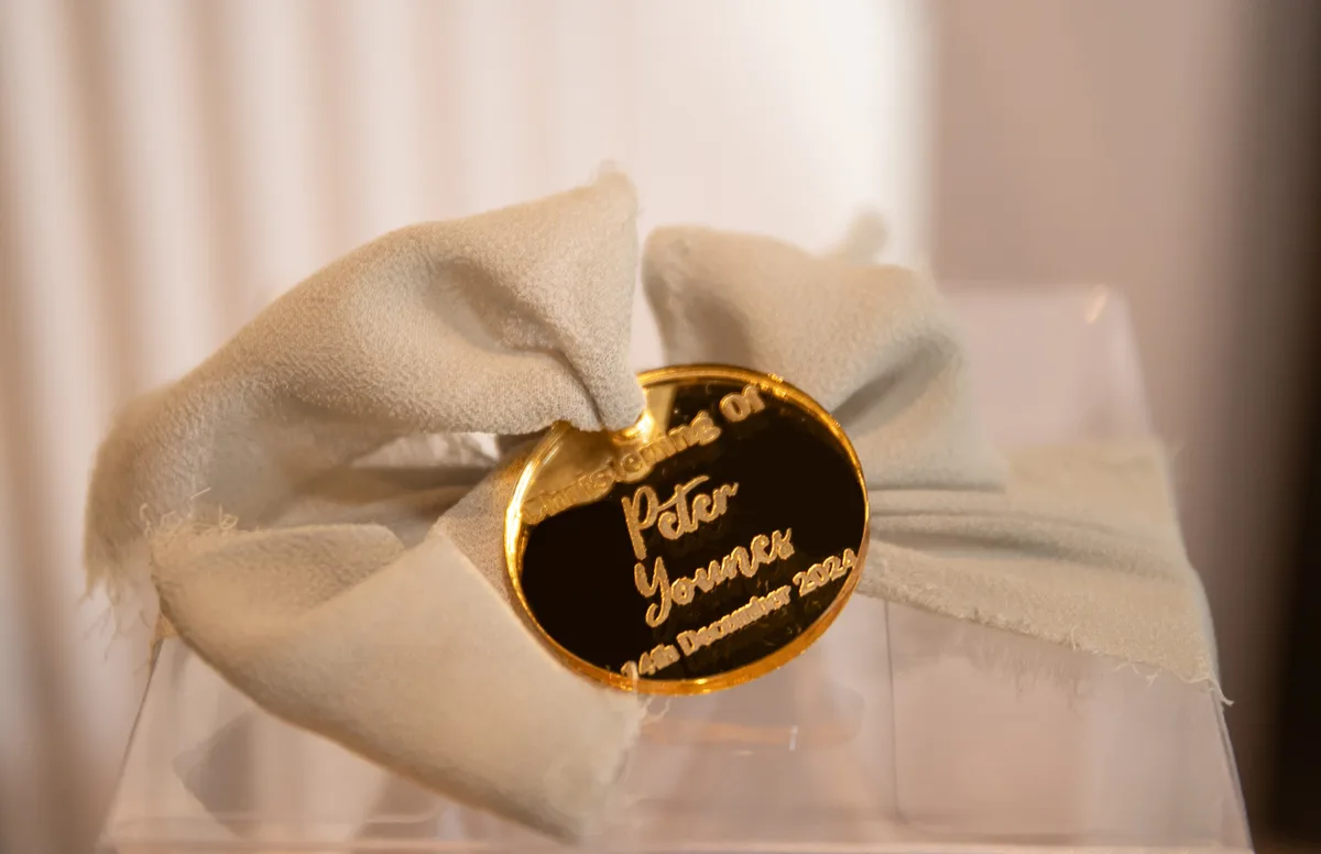 A personalised gold tag tied to a clear favour box with a white bow